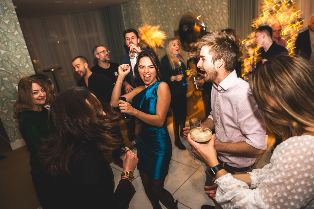 Wide shot of a Christmas party in full swing, tree lights in the background
