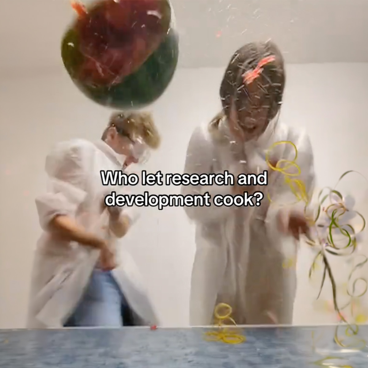A watermelon exploding above two people in lab coats, confetti everywhere