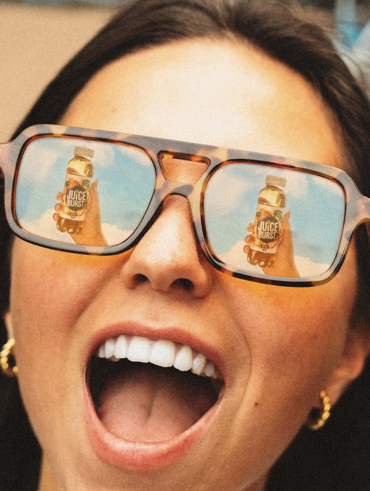 Close up of sunglasses reflecting two Juice Burst bottles against a blue sky